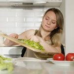 A woman preparing a fresh salad with lettuce and tomatoes in a modern kitchen.